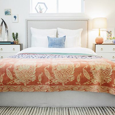 A bedroom in an apartment with a double bed and beside cabinets, and a vivid patterned bedspread.